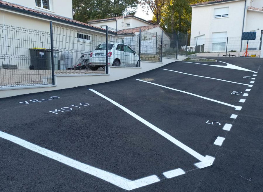 Marquage au sol neuf d&rsquo;un parking r&eacute;sidentiel avec places num&eacute;rot&eacute;es et fl&egrave;ches de circulation devant une maison cl&ocirc;tur&eacute;e.