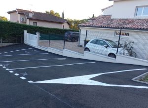 Marquage au sol neuf d&rsquo;un parking r&eacute;sidentiel avec places num&eacute;rot&eacute;es et fl&egrave;ches de circulation devant une maison cl&ocirc;tur&eacute;e.